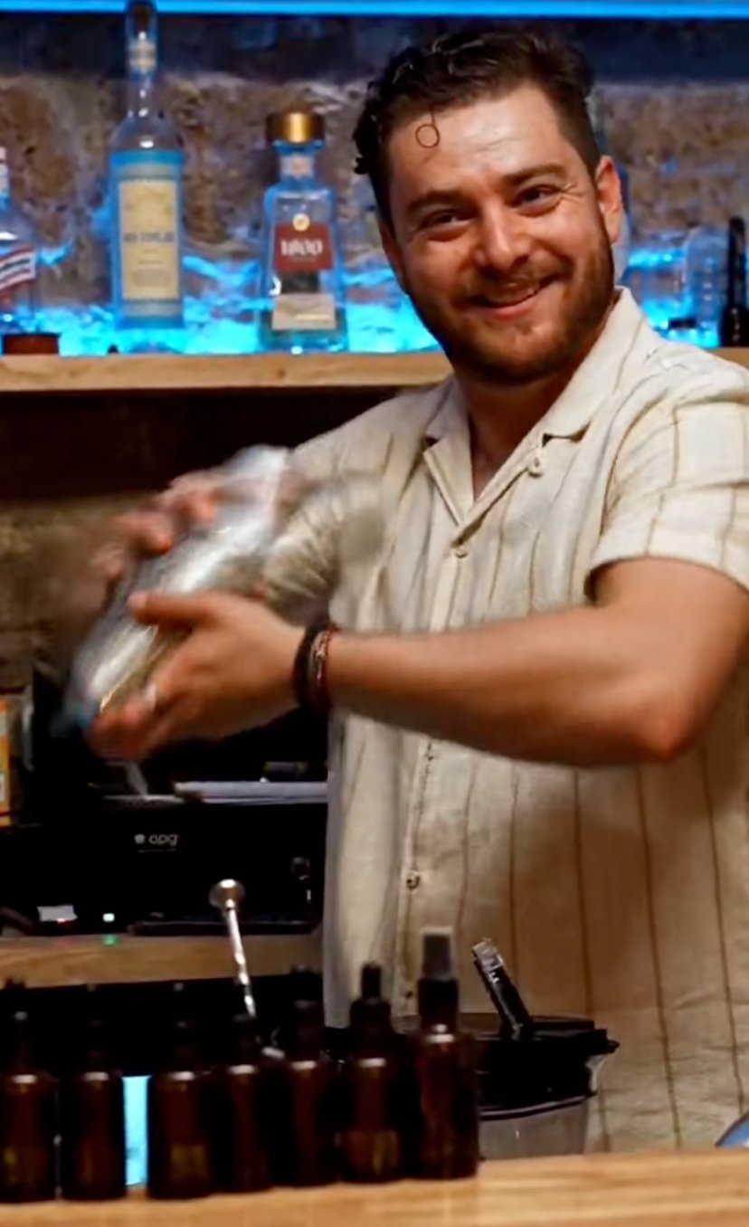 Jalil, souriant, prépare un cocktail au shaker derrière le bar